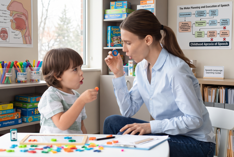A speech therapist demonstrates mouth movements to a young boy during a specialized motor-planning session for Childhood Apraxia of Speech.