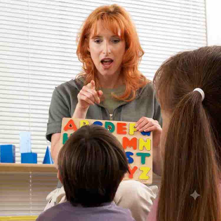 An educator teaches phonetic consistency and letter recognition to young children using an interactive alphabet puzzle in a classroom.
